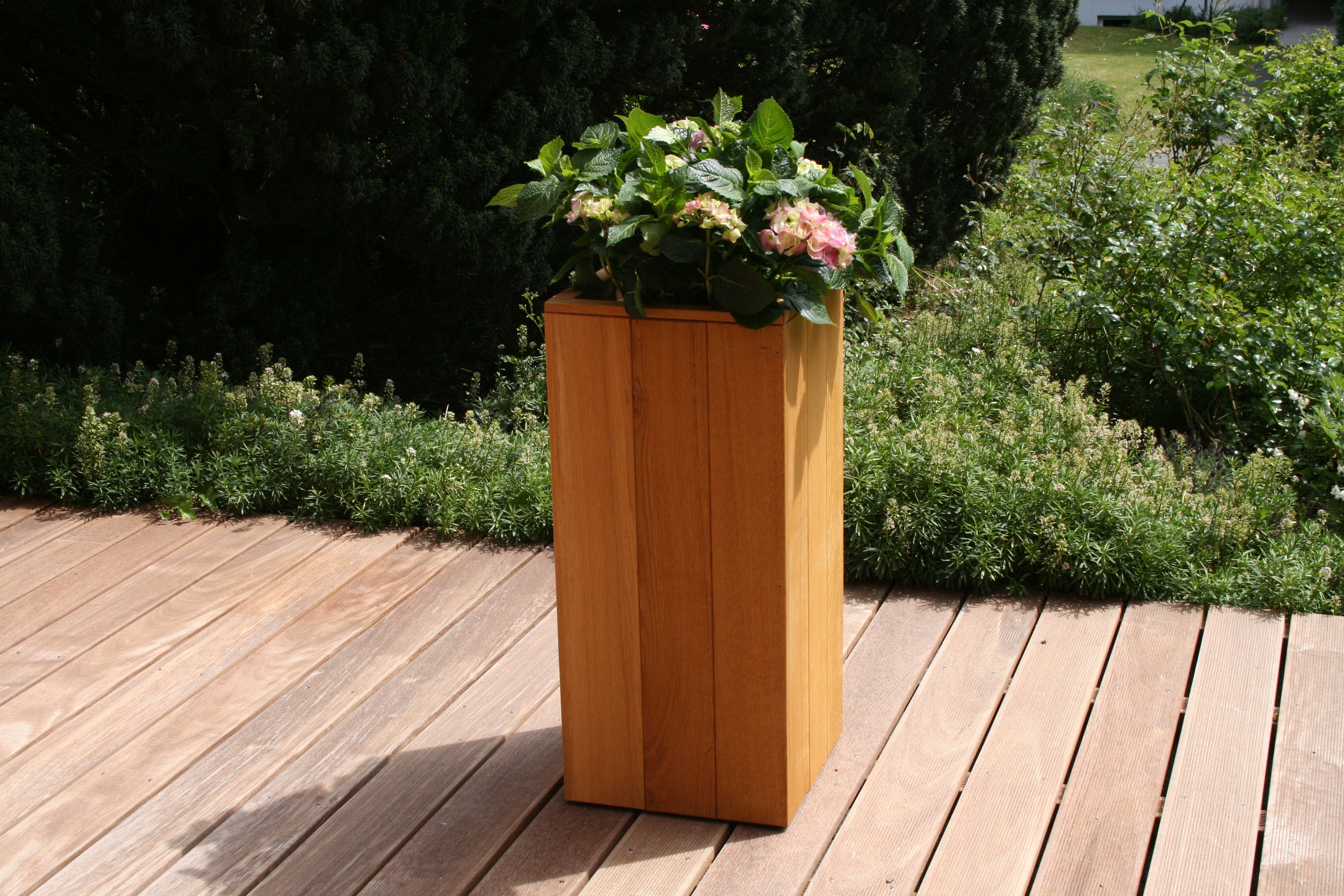 Holzterrasse aus IPE-Terrassendielen, 1-seitig geriffelt, 21 x 145 mm, im Außenbereich mit Blumenkübel aus Holz und grünem Pflanzbeet im Hintergrund
