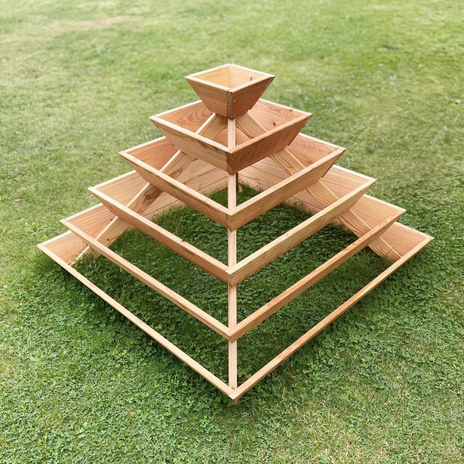 Pyramidenförmige Pflanzenstruktur aus naturbelassenem Lärchenholz mit mehreren Ebenen auf einer Rasenfläche, geeignet für Kräuteranbau, inklusive Vlies, Abmessungen 120 x 120 x 87 cm.