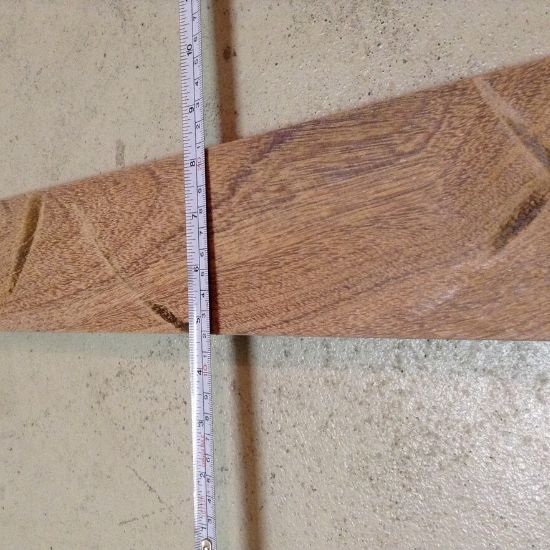 Schmale Holzlatte mit deutlicher Maserung liegt quer auf hellem Betonboden, ein ausgeklappter Metall-Zollstock mit Zentimeter-Einteilung liegt längs an der Latte zur Längenmessung