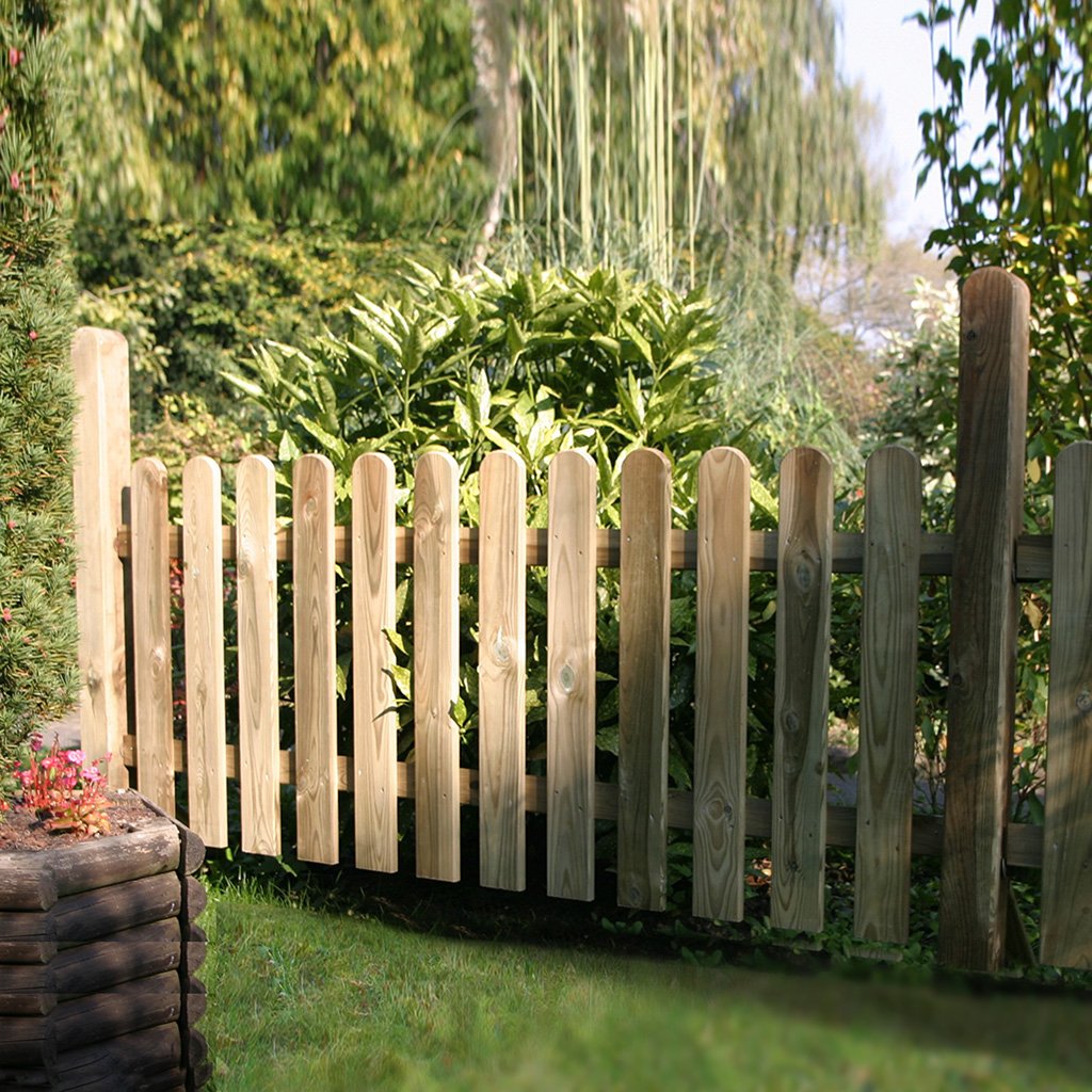 Holz-Staketenzaun im Garten, kesseldruckimprägniert, mit senkrechten, abgerundeten Latten, vor dichten grünen Sträuchern und Pflanzen stehend, Produkt: Vorgartenzaun L.18 x 90 mm, R. 22 x 70 mm