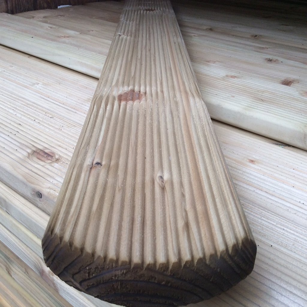 Nahaufnahme eines kesseldruckimprägnierten Zaunbretts Mosel mit Rundkopf und geriffelter Oberfläche, Maße 22 x 95 mm, auf einem Stapel ähnlicher Holzbretter liegend