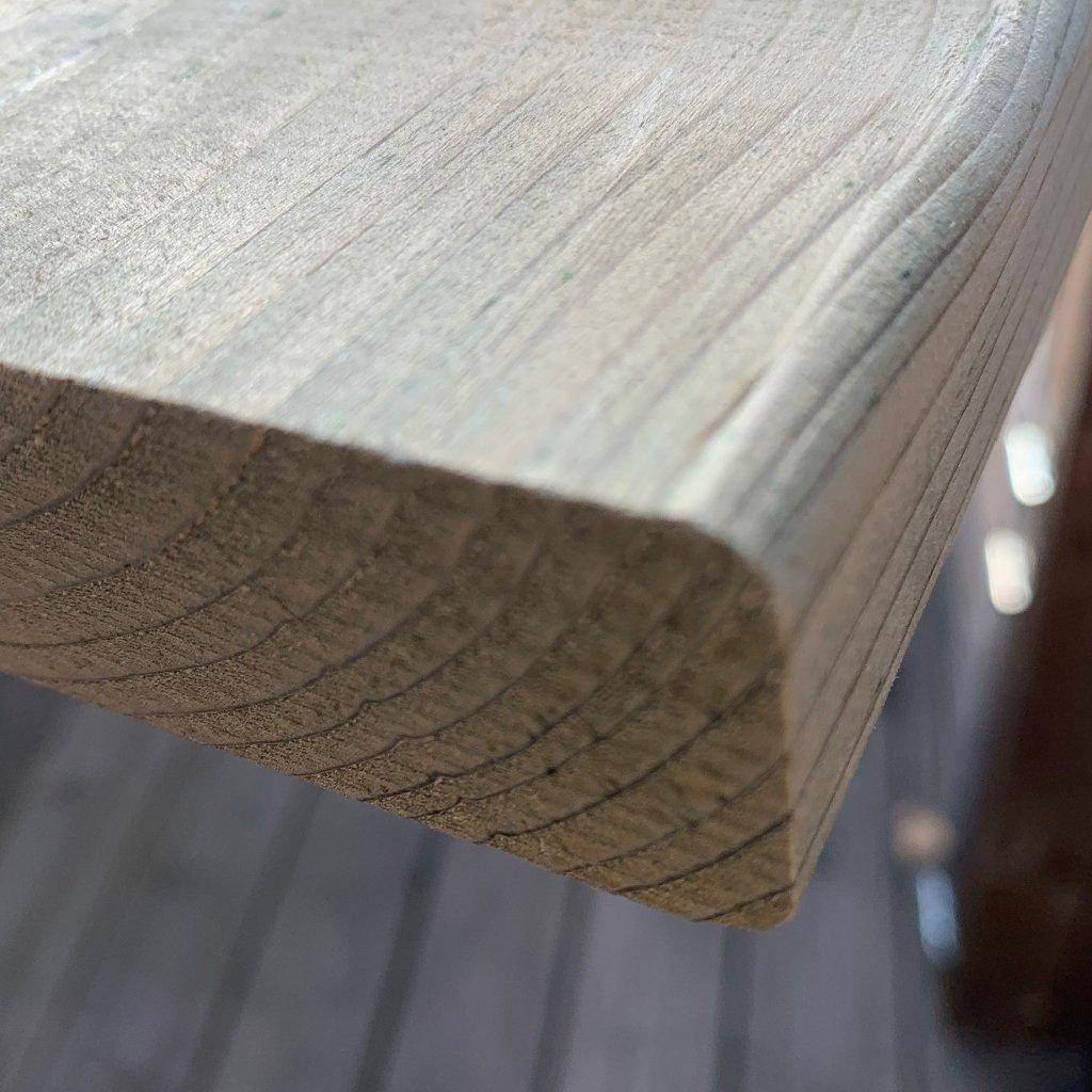 Nahaufnahme eines Fichtenbretts (28×142×1800 mm), kammergetrocknet und gehobelt, mit abgerundeter Kante und kesseldruckimprägniertem, leicht grünlich getöntem Holz; sichtbare Jahresringe an der Stirnseite