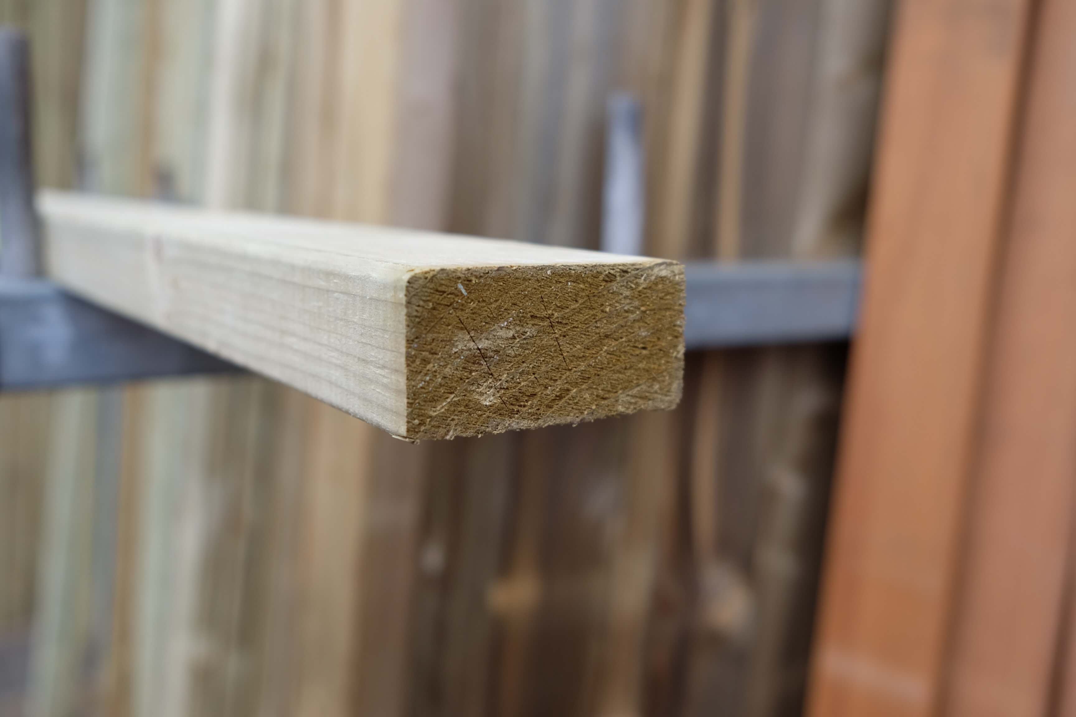 Nahaufnahme eines glatt gehobelten, gefasten Konstruktionsholzes mit den Maßen 20x45 mm, kesseldruckimprägniert, vor unscharfem Hintergrund mit weiteren Holzlatten