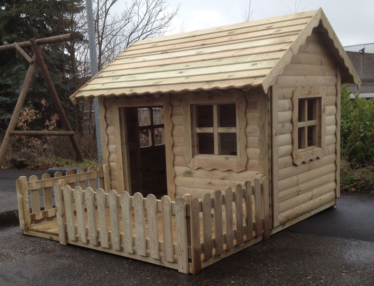Holzspielhaus für Kinder, Modell Diana, Größe 170 x 220 x 155 cm, kesseldruckimprägniert, mit überdachtem Eingang, zwei Fenstern und kleiner Veranda mit Holzzaun, im Außenbereich aufgestellt