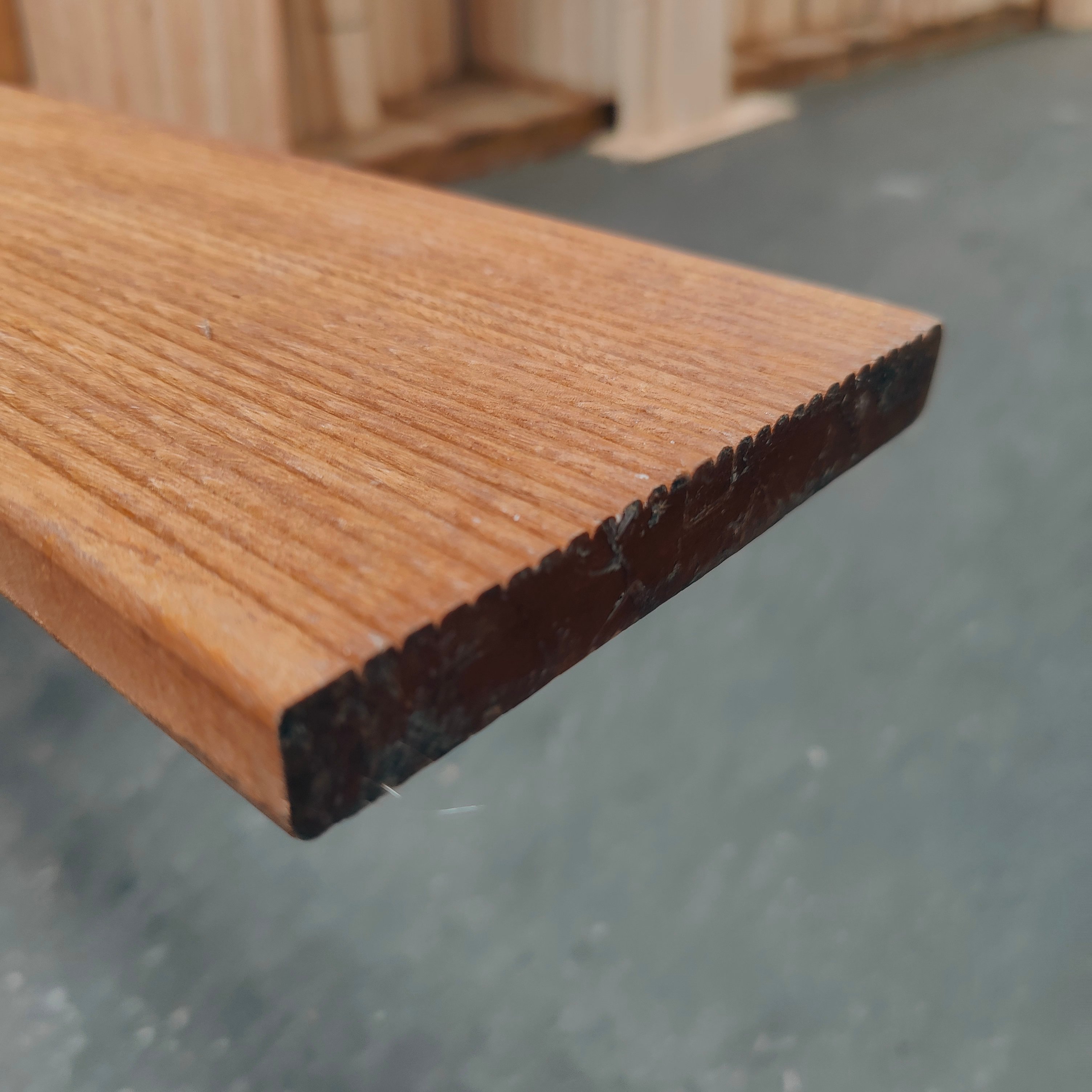 Nahaufnahme einer Bangkirai Terrassendiele mit den Maßen 25 x 145 x 3960 mm, einseitig geriffelt, sichtbare Maserung und Stirnkante, Holzdielen im Hintergrund, Fokus auf Struktur und Kantenprofil