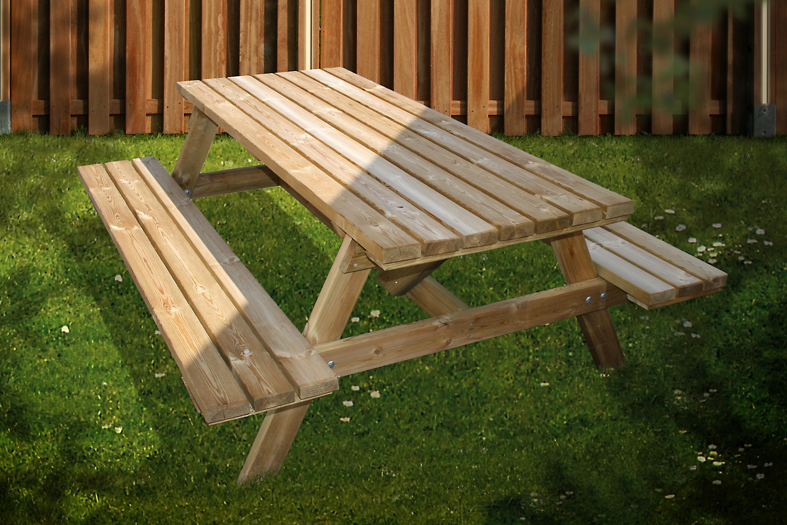Holz-Picknicktisch mit zwei Bänken auf Rasen vor einem Holzlattenzaun, Sonnenschatten auf der Tischfläche